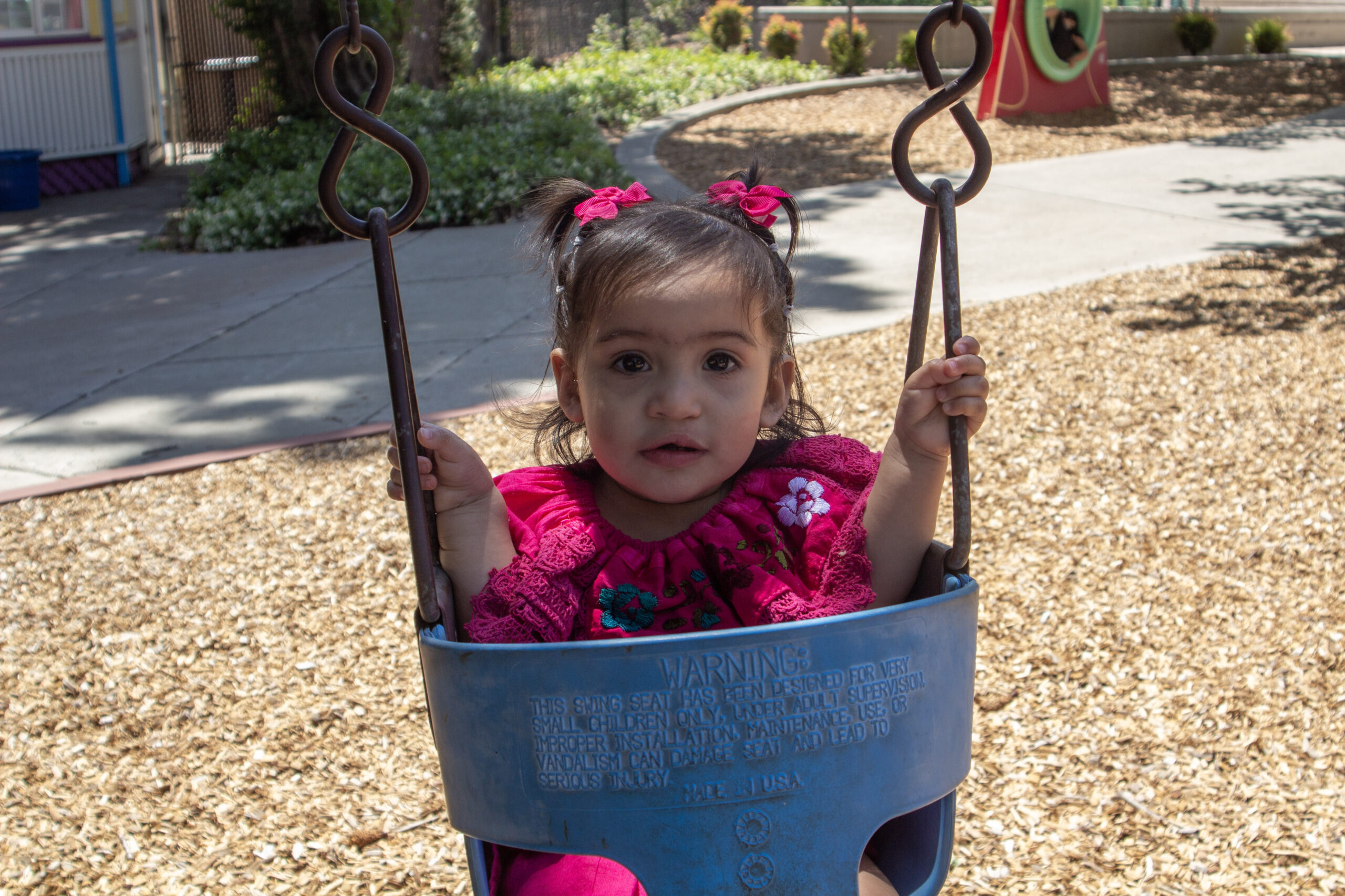 Emarosa hsa pigtails and is swinging in a swing at a park.