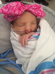 Baby Kynslee with a pink bow and wrapped in a hospital blanket.