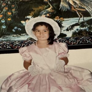 Vanessa as a young child in a dress and a hat looking at the camera.